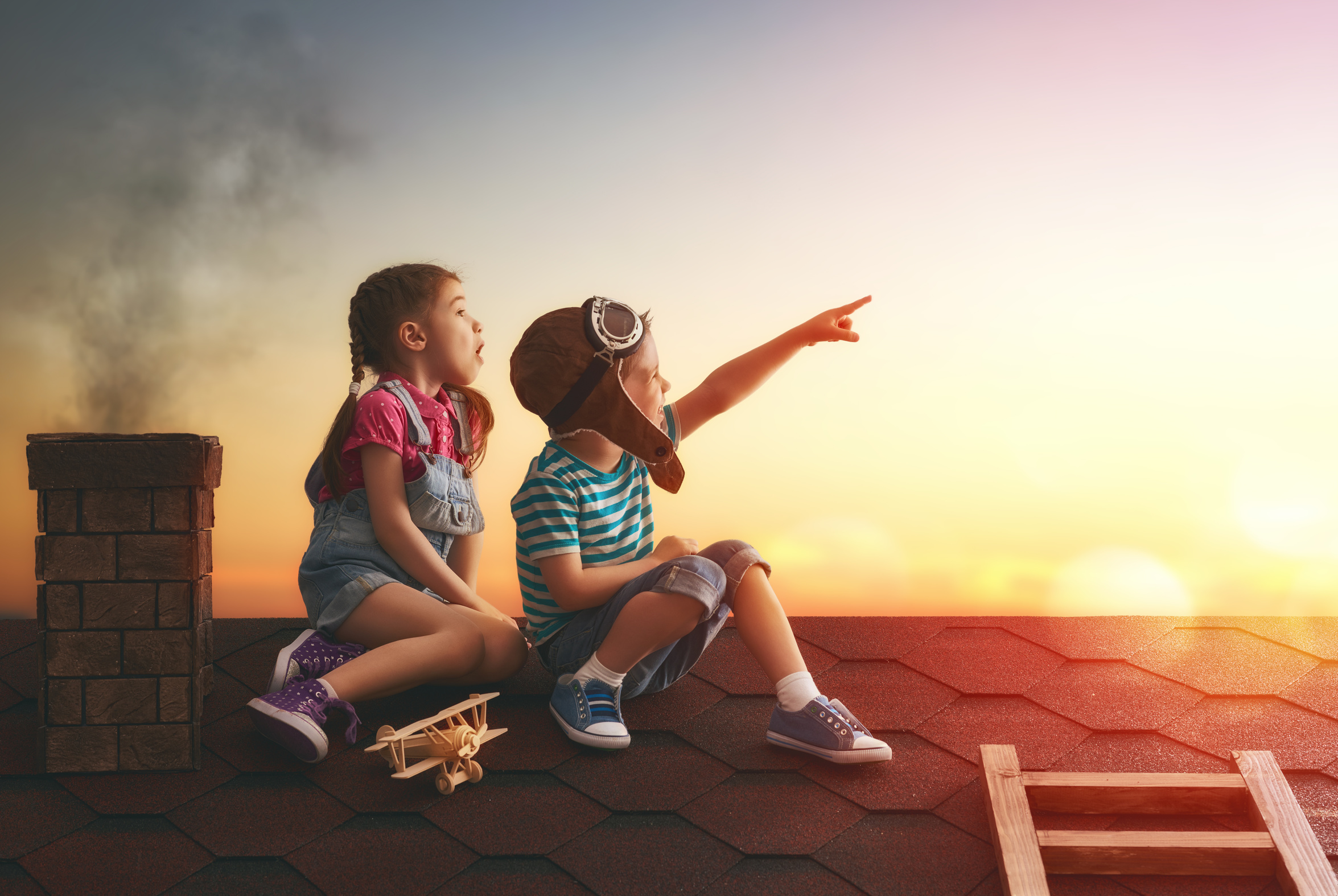 Two little children playing on the roof of the house and looking at the sky and dreaming of becoming a pilots.